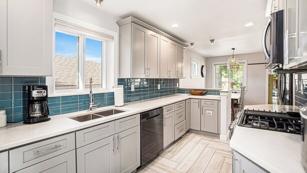 A modern kitchen with white cabinets, a dishwasher, a stove, and a large window providing natural light. - Backyard Wonderland: Ultimate Outdoor Fun (Denver)
