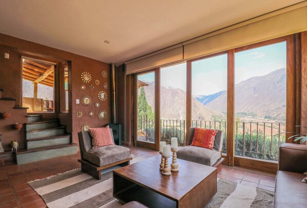 A spacious living room with a large window offering a mountain view, a staircase leading to an upper level, and a cozy seating area with a coffee table.