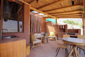 A wooden interior with a kitchen area, a dining table, and wicker chairs.