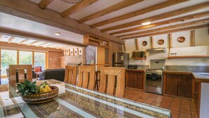 A spacious kitchen with wooden beams, a large dining table, and a view of the outdoors.