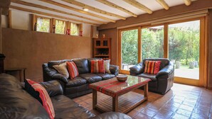 A spacious living room with leather sofas, a wooden coffee table, and large windows offering a view of the outdoors.