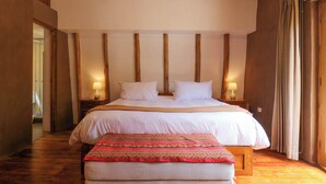 A bedroom with a large bed, wooden beams on the ceiling, and a nightstand with a lamp.