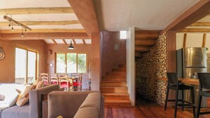 Ein gemütliches Wohnzimmer mit einer Holztreppe, einem Essbereich inklusive Kühlschrank und einem großen Fenster für natürliches Licht.