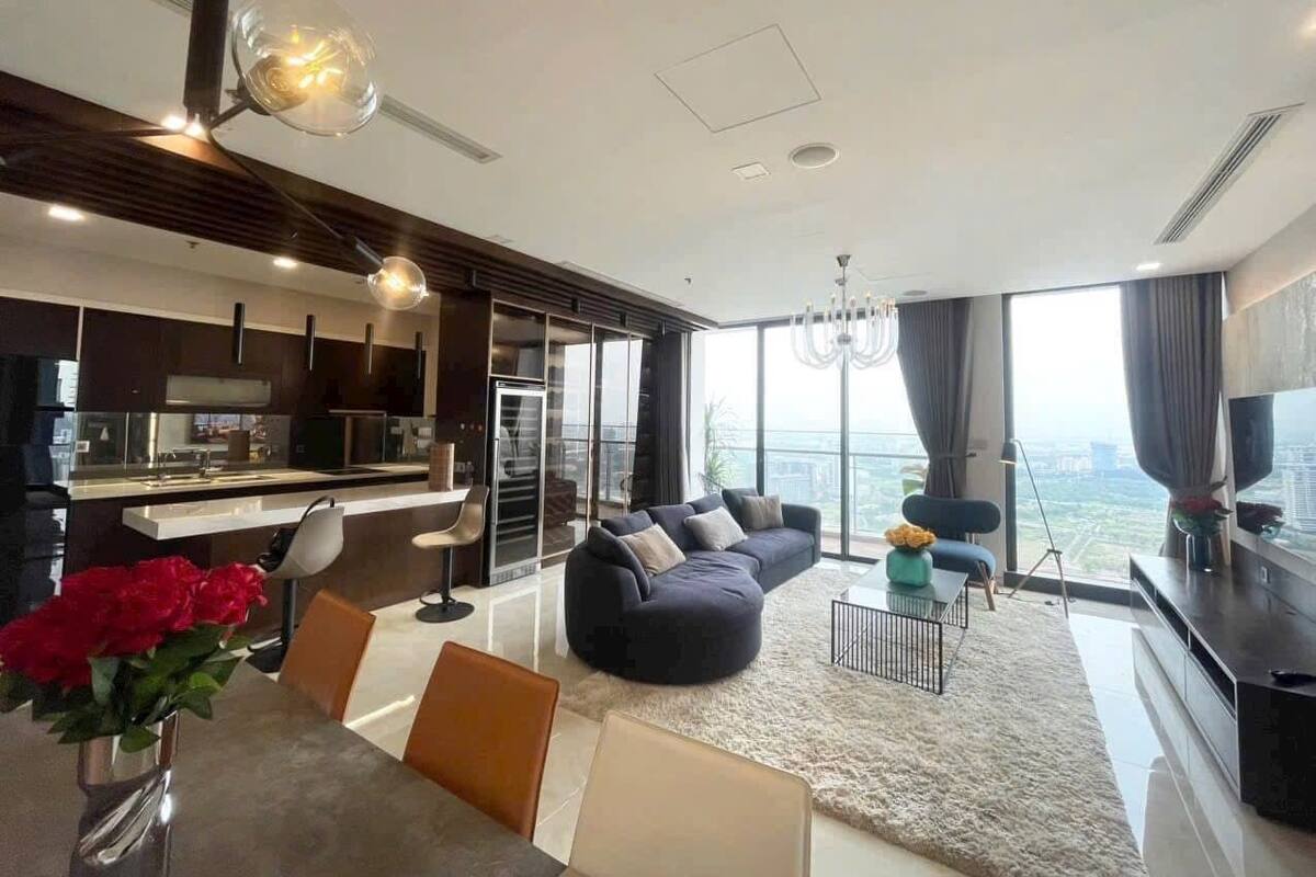 Una sala de estar moderna con un sofá, un comedor con mesa y sillas, una cocina y un amplio ventanal con vistas a la ciudad.