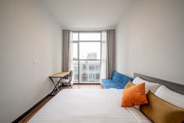 A hotel room with a large bed, a desk, and a view of buildings through a window. - Metropole - Christine Hospitality (Ho Chi Minh City)