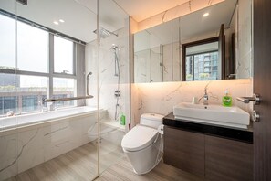 Ein modernes Badezimmer mit Duschabtrennung aus Glas, einer weißen Toilette, einem Waschbecken mit Spiegel darüber und einem Fenster mit Blick nach draußen.