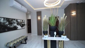 A modern interior with a bench, a table with decorative items, and a large abstract painting. - Arjan Park Hotel Wadi Ad Dawasir (Wadi-Ad-Dawasir)