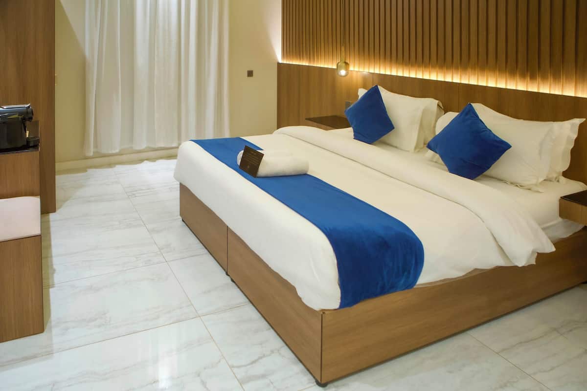 A modern hotel room with a wooden bed, white bedding, and a blue accent.