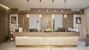 A reception desk with a marble top, wooden paneling, and a clock above it. - Arjan Park Hotel Wadi Ad Dawasir (Wadi-Ad-Dawasir)