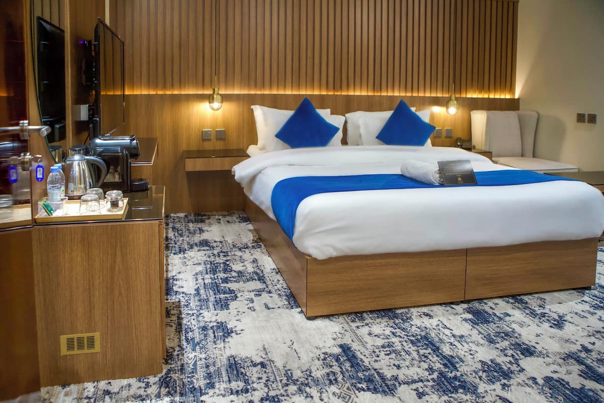 A hotel room with a large bed, wooden headboard, bedside tables, a coffee machine, and a TV.