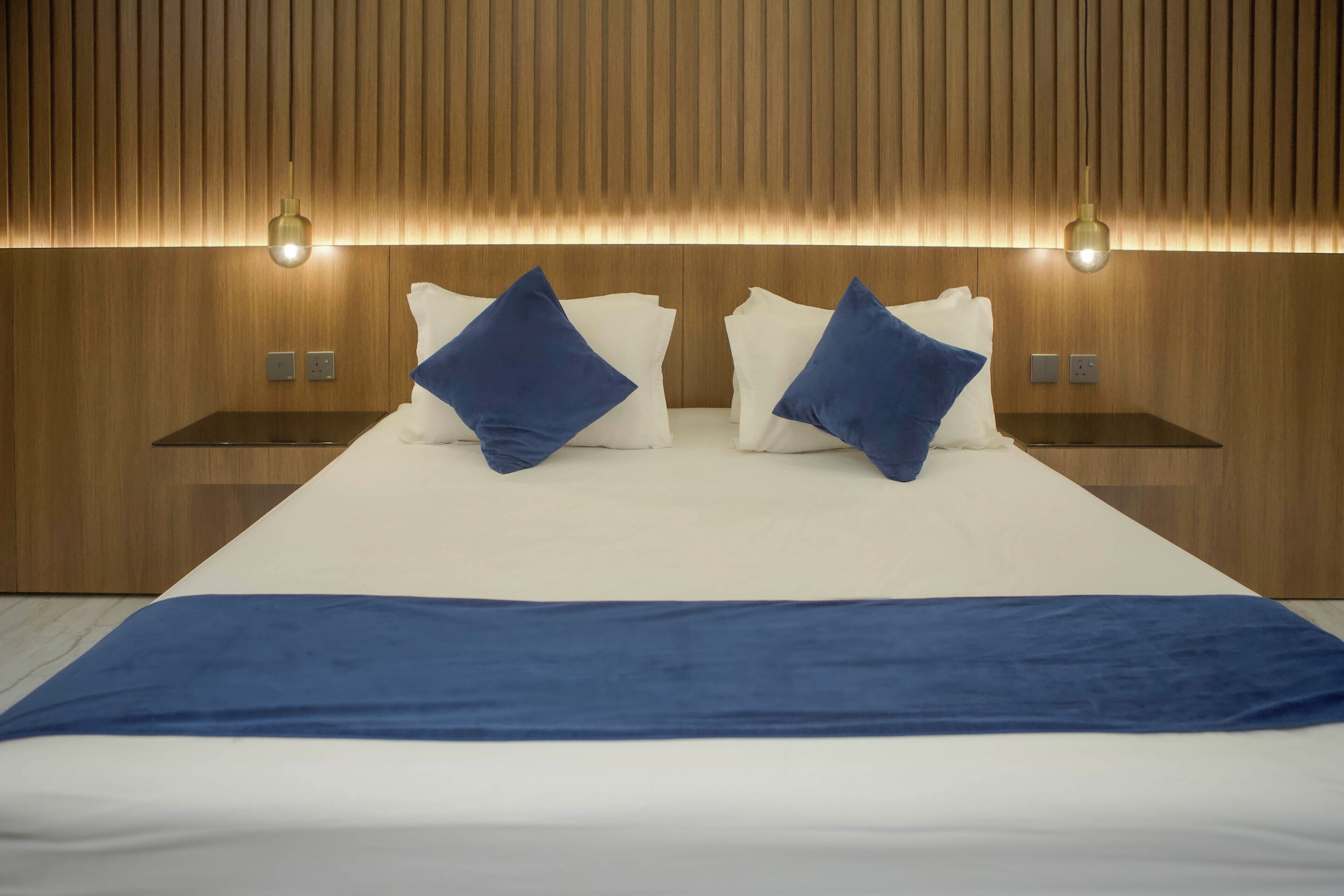 A modern hotel room with a large bed, two bedside tables, and a wooden wall paneling.