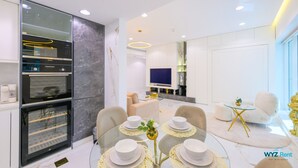 A modern living room with a glass dining table, white sofas, and a built-in entertainment system. - 1 BR in Marina (Dubai)