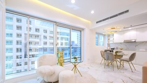 A modern apartment with large windows, a dining area with a glass table, and a kitchen with white cabinets. - 1 BR in Marina (Dubai)
