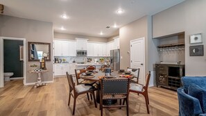 A modern kitchen with white cabinets, a stainless steel refrigerator, and a dining area with a wooden table and chairs. - AT&T + Globe Life Walkable | Prime Group Stay (Arlington)