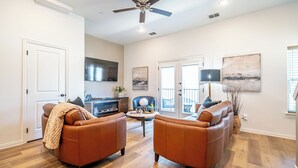 A spacious living room with two leather sofas, a fireplace, and a ceiling fan. - Chic Townhome | Walk to AT&T Stadium + Globe Life (Arlington)