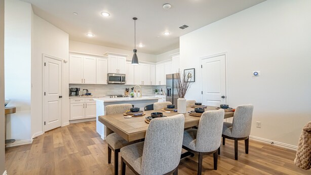 A modern kitchen with white cabinets, a stainless steel refrigerator, and a dining area with a wooden table and upholstered chairs. - Chic Townhome | Walk to AT&T Stadium + Globe Life (Arlington)