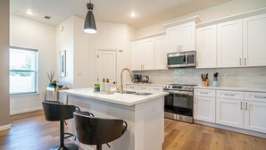A modern kitchen with white cabinetry, a central island with a sink, a stainless steel oven, and a microwave above the stove. - Chic Townhome | Walk to AT&T Stadium + Globe Life (Arlington)