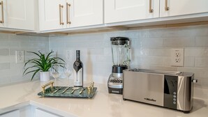 A kitchen with white cabinets, a blender, a toaster, and a wine bottle. - Chic Townhome | Walk to AT&T Stadium + Globe Life (Arlington)