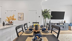 Un comedor con una mesa negra, paredes blancas y un televisor montado en la pared.