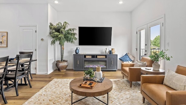 Una sala de estar moderna con comedor, un televisor grande montado en la pared y una planta en maceta.