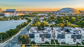 Una zona residencial moderna con viviendas compactas, un estadio grande y un edificio comercial al fondo.