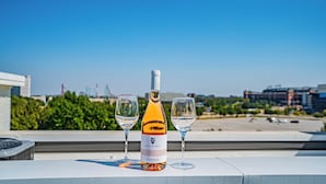 Una botella de vino y dos copas en una terraza en la azotea, con un paisaje urbano de fondo.