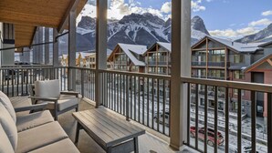 A balcony with wooden furniture, a view of snow-covered mountains, and a clear sky. - Mountain Therapy | Just Be Here (Canmore)