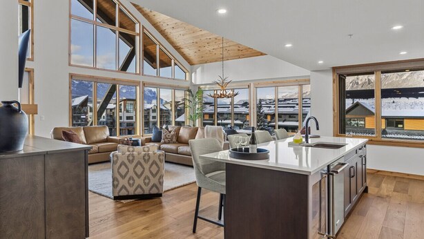A modern kitchen with a central island, large windows with mountain views, and a cozy seating area. - Mountain Therapy | Just Be Here (Canmore)