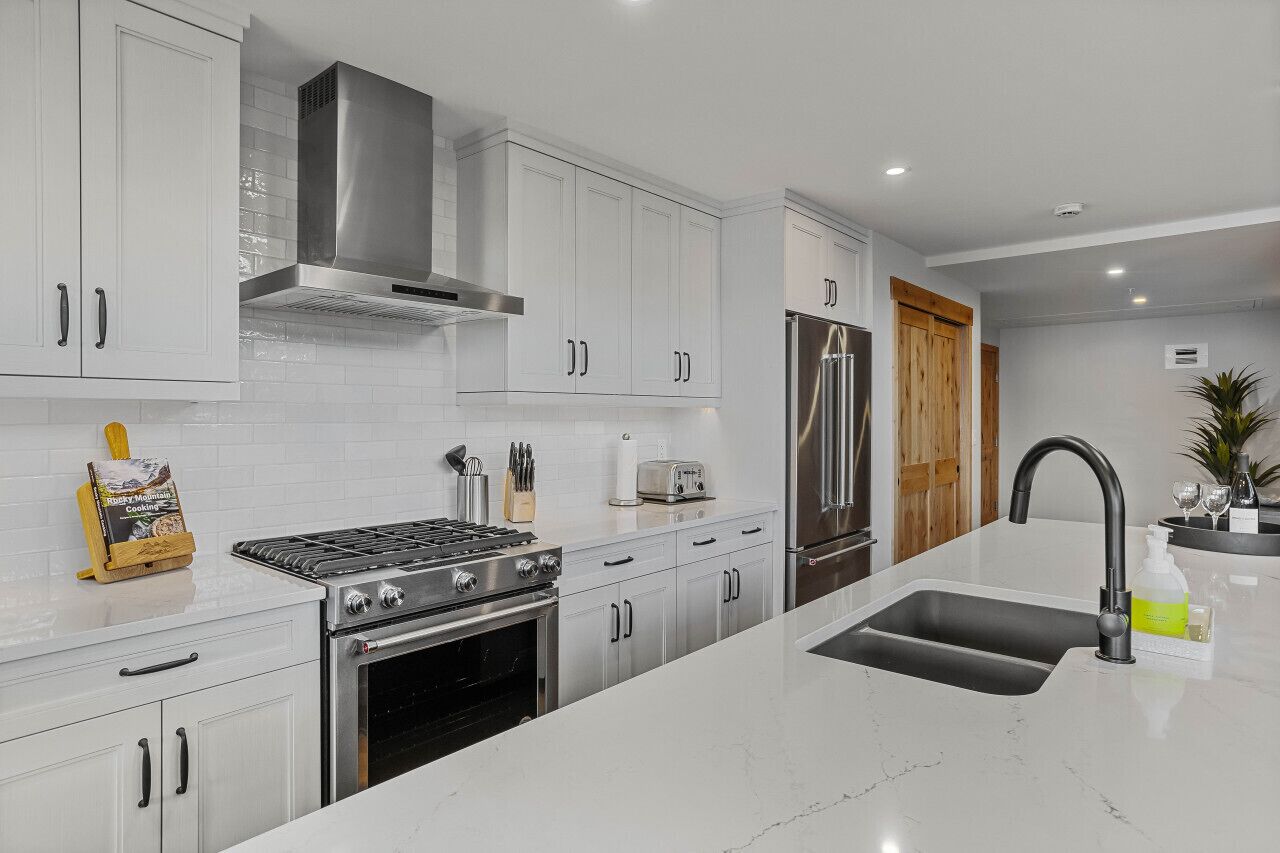 A modern kitchen with white cabinetry, stainless steel appliances, a central island with a sink, and a built-in oven.