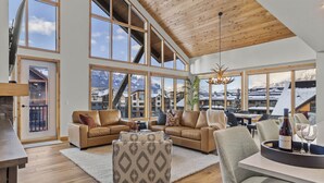 A spacious living room with large windows, a wooden ceiling, and a view of mountains. - Mountain Therapy | Just Be Here (Canmore)