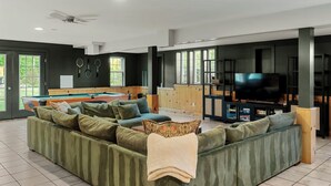 Ein geräumiges Wohnzimmer mit Pooltisch, grünem Sofa und einem Flachbildfernseher.