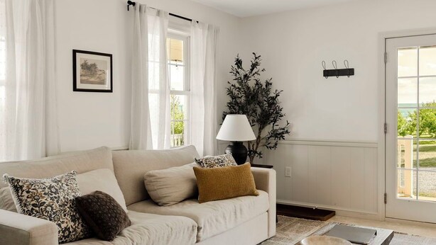 Ein Wohnzimmer mit einem beigefarbenen Sofa, einem Holztisch, einer Lampe und einer Pflanze.