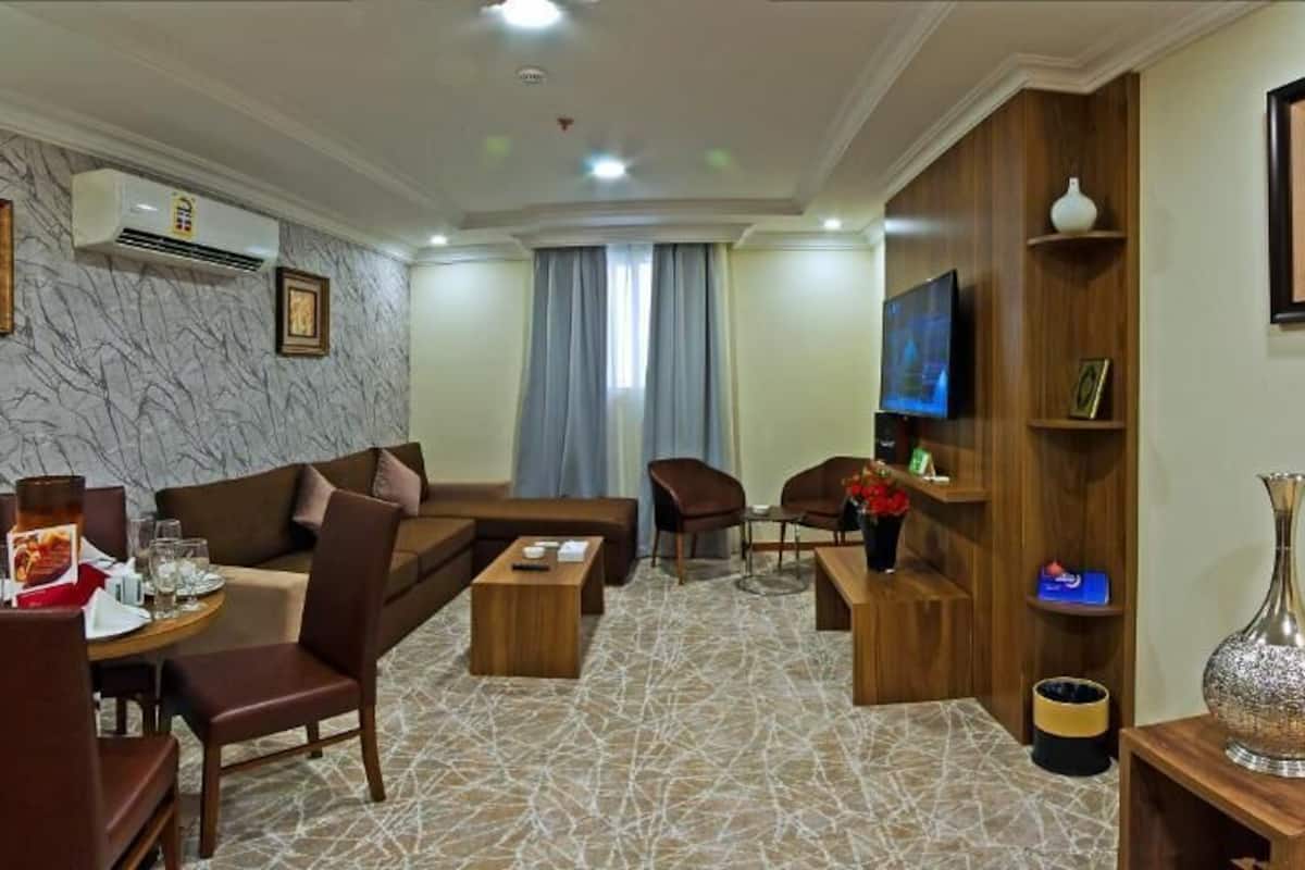 A modern living room with a sofa set, a coffee table, and a TV. There is a wooden sideboard with decorative items and a vase.
