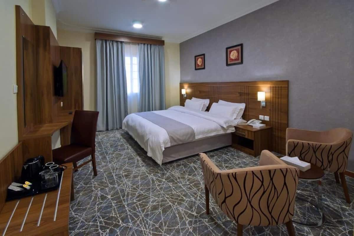 A hotel room with a bed, a desk, a chair, a TV, and a window with curtains.