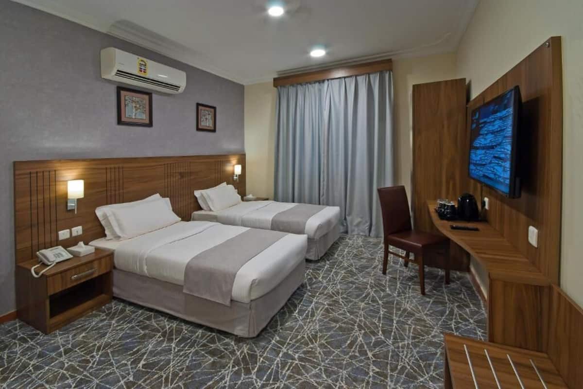 A hotel room with two beds, a desk, a chair, a TV, and an air conditioning unit.
