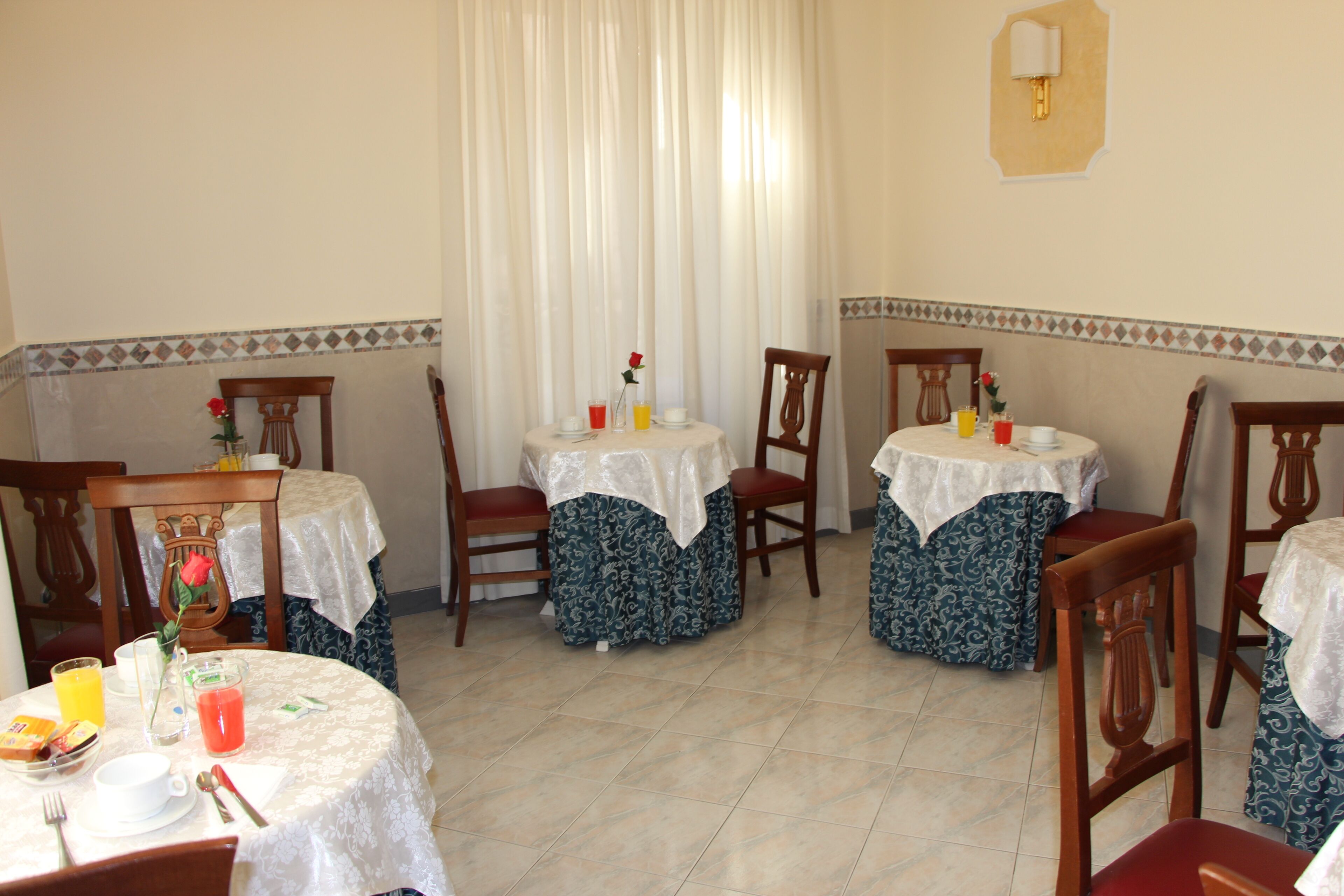 Un espace repas avec quatre tables rondes, chacune recouverte d’une nappe blanche et agrémentée d’une seule chaise. Des compositions florales décorent les tables, et une variété d’articles de table, notamment des tasses, des assiettes et des couverts, y sont disposés.