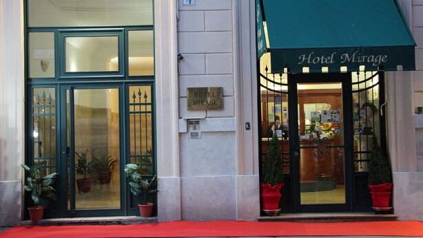 Entrada de hotel con toldo verde, identificación que dice "Hotel Mirage", el número "4" y plantas en macetas en las puertas.