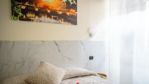 Un dormitorio con cabecera de mármol, cama con ropa de cama estampada y un cuadro colgado en la pared que representa un atardecer.