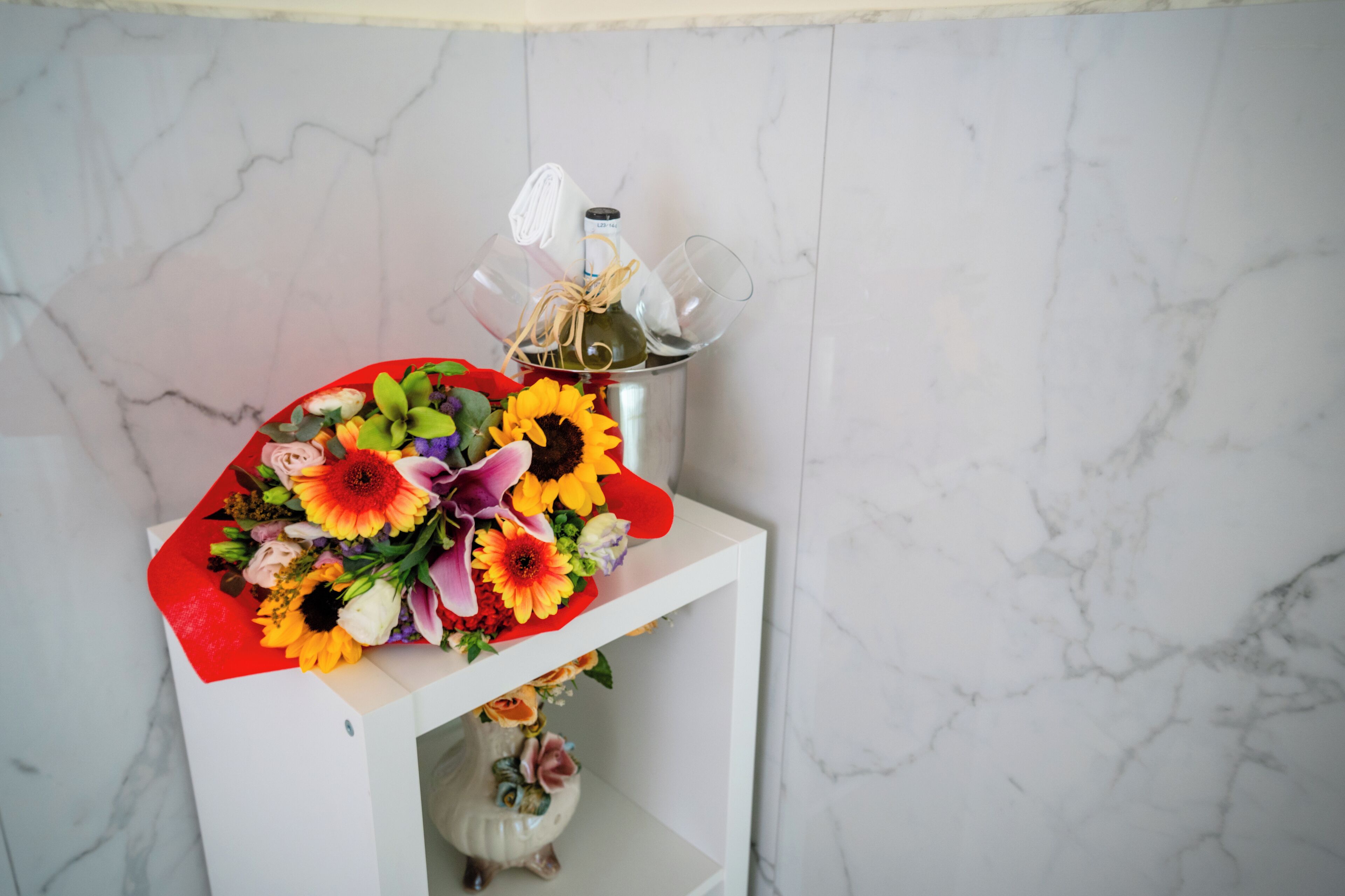 Une étagère blanche ornée d’un bouquet de fleurs, d’une bouteille et d’un verre.