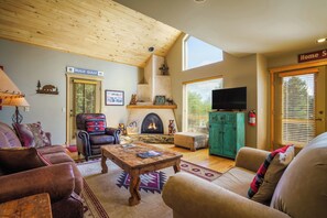 A cozy living room with a fireplace, leather sofas, a wooden coffee table, and a television. - Bear Paw Place by Velo (Angel Fire)
