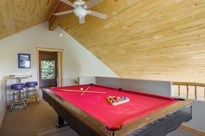 A pool table with a red felt surface, a ceiling fan, and wooden beams. - Bear Paw Place by Velo (Angel Fire)