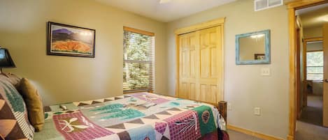 A bedroom with a large bed, a ceiling fan, a window with blinds, a door, and a framed picture on the wall.