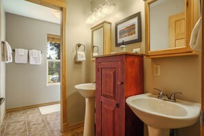 A bathroom with two sinks, a wooden cabinet, a mirror, and a window.