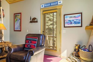 Ein Wohnzimmer mit einer Ledersofa, einem Holztisch und einem gerahmten Bild eines Bären. Eine Tür mit einem Schild darüber und ein Fenster mit Jalousien sind ebenfalls vorhanden.