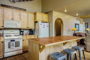 A kitchen with wooden cabinets, a white stove, a refrigerator, and a wooden island with stools.
