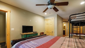 A bedroom with a bed, a TV, a ceiling fan, and a door.
