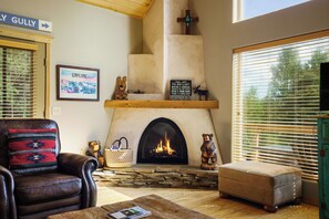 Ein gemütliches Wohnzimmer mit Kamin, Ledersessel, einer hölzernen Bank und einem gerahmten Bild an der Wand.