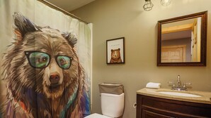 A bathroom with a toilet, sink, and mirror. There is a framed picture of a bear on the wall.