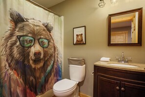 A bathroom with a toilet, sink, and mirror. There is a framed picture of a bear on the wall.