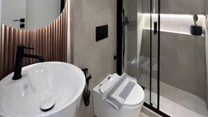 A modern bathroom with a large white sink, a toilet, and a glass shower enclosure. - BlueMotion - PortSuite (Piraeus)